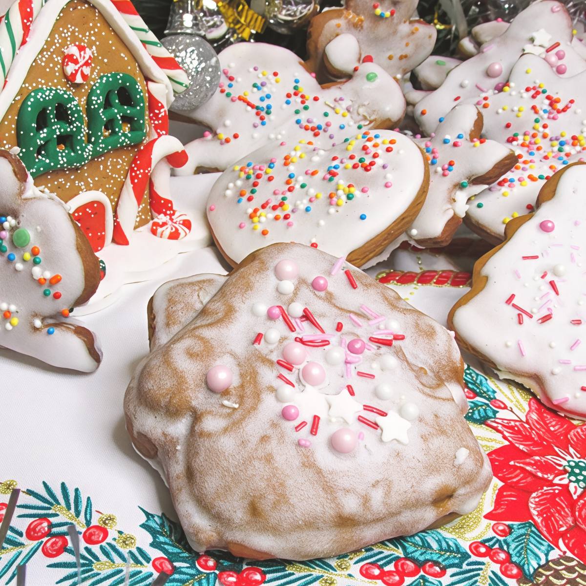Traditional Russian Kozuli gingerbread cookies iced with white icing and colorful sprinkles placed near a decorated gingerbread house, served as a festive European Christmas dessert.