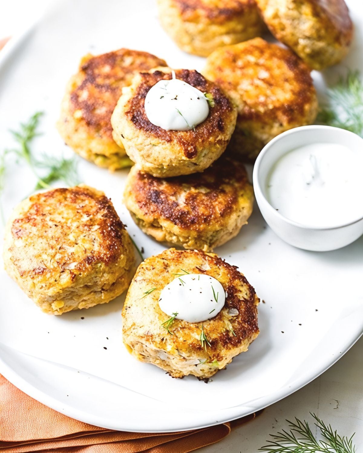 Crispy Salmon Croquettes with Dill Sauce topped with creamy sauce and fresh dill sprigs alongside a dipping bowl, featured as a delicious high protein low carb recipes dinner.