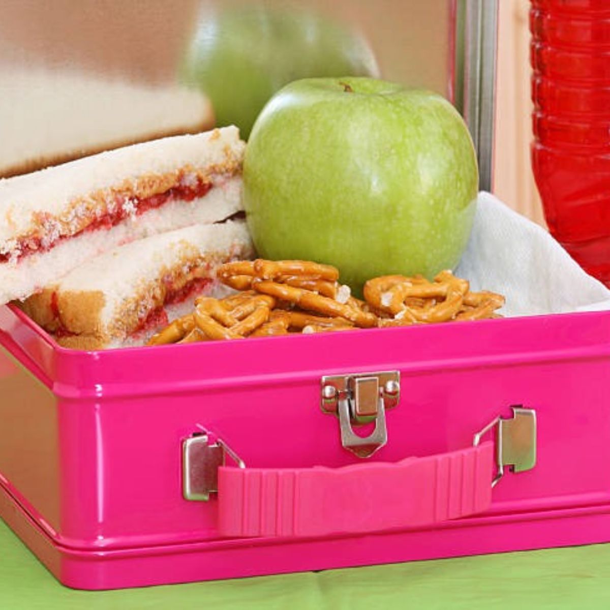 An old metal lunchbox holding a wrapped sandwich beside a modern insulated bag and frozen cold sources on the counter.