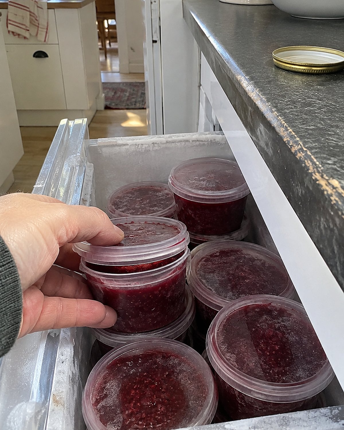 Small containers of red fruit jam sit in an open freezer drawer.