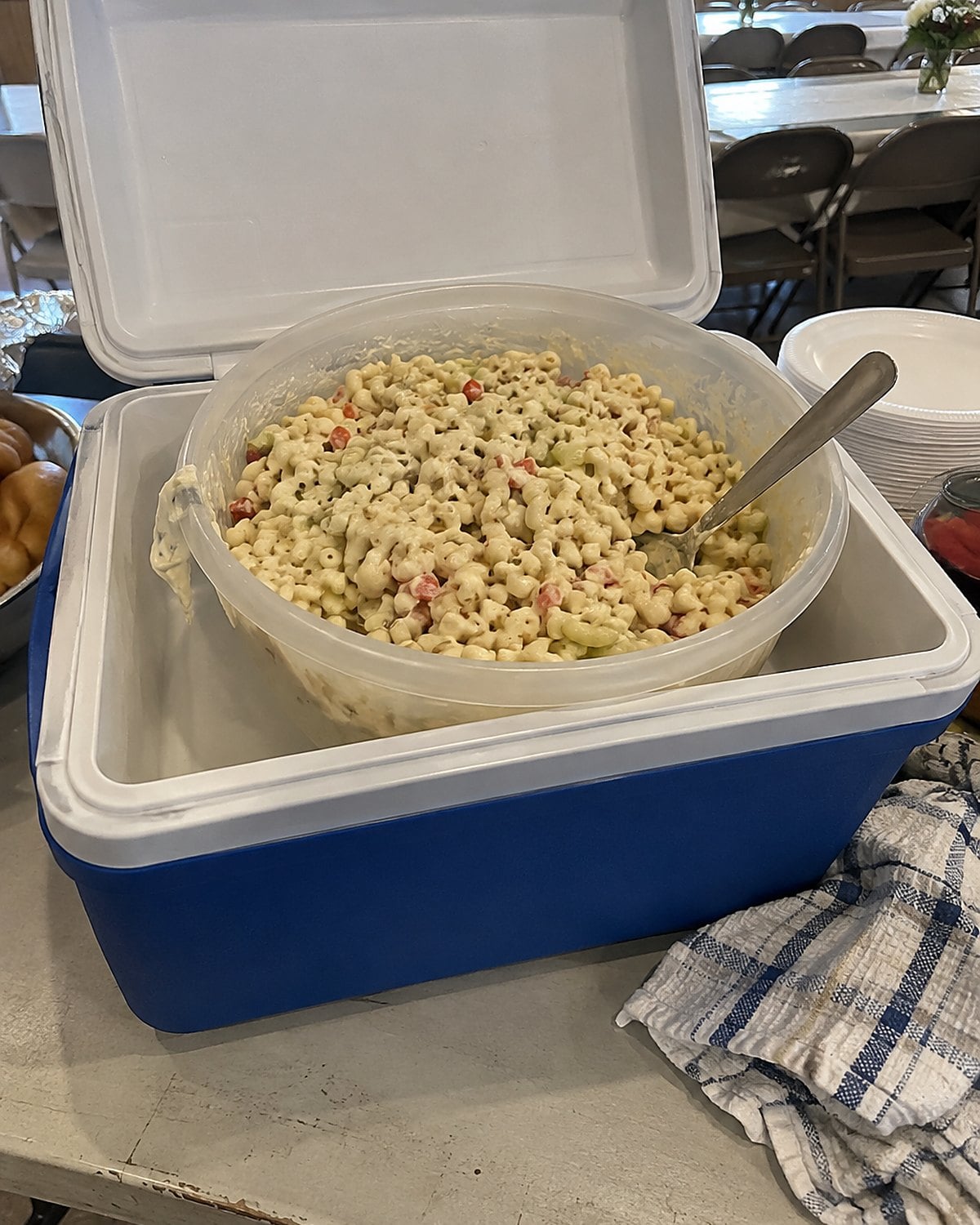 A large bowl of macaroni salad sits in a cooler on a church hall table.