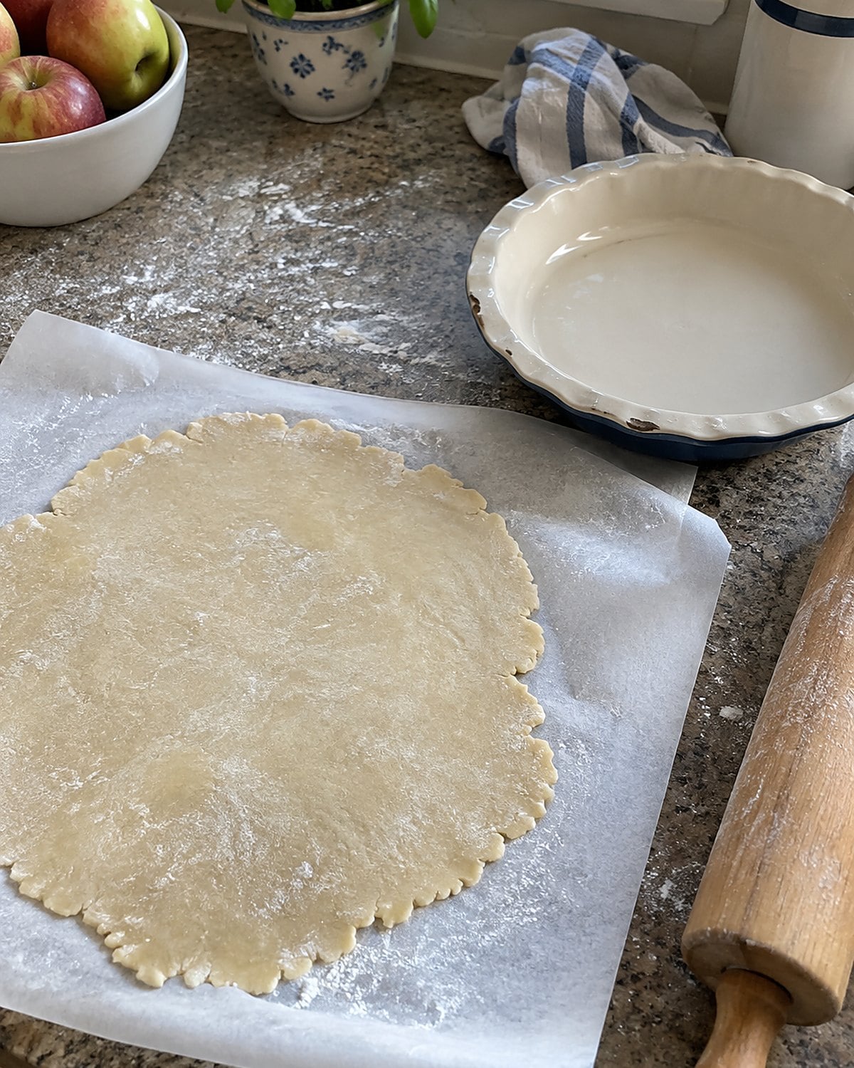 Pie dough lies between two sheets of parchment beside a chipped pie plate.