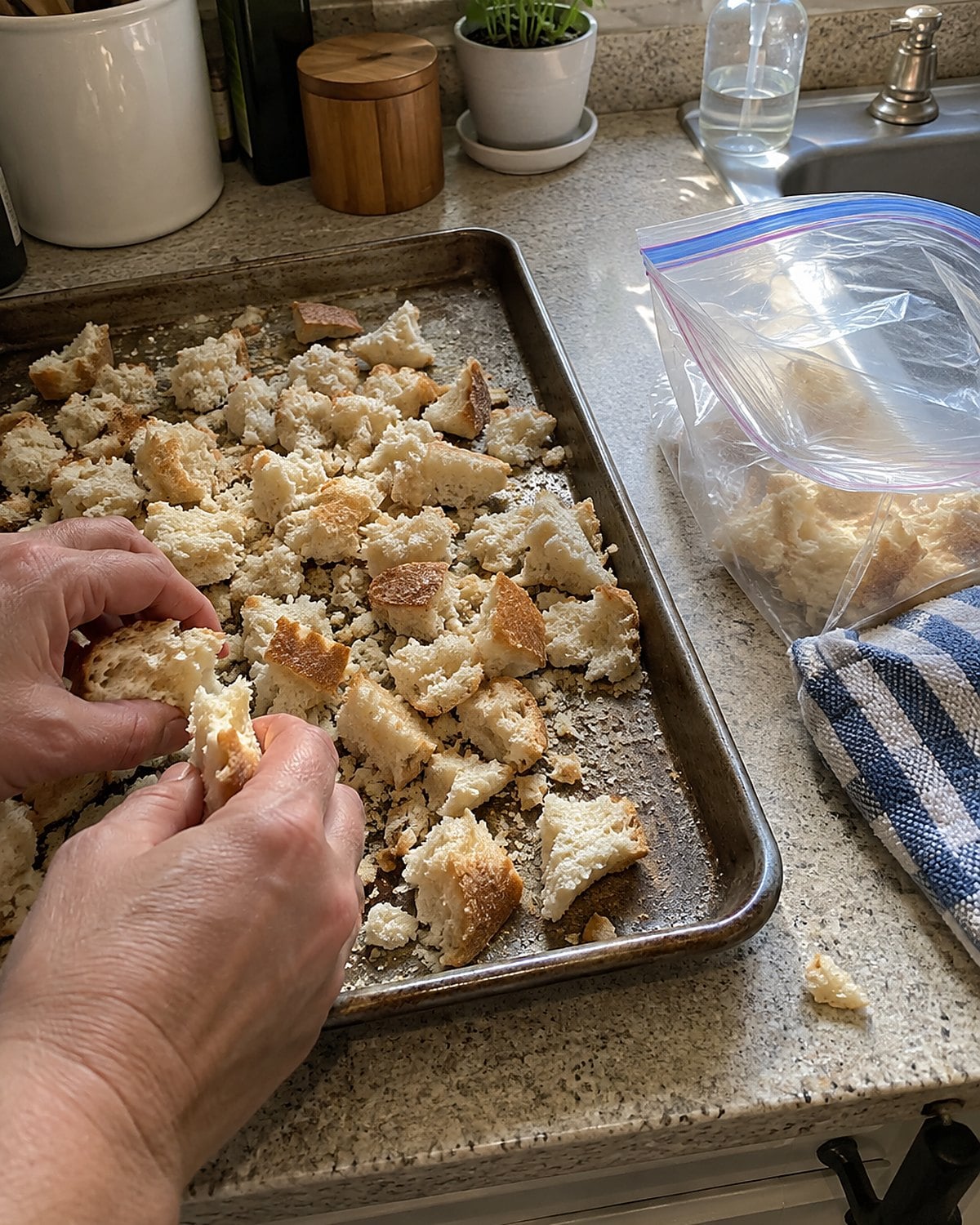 Torn stale bread and coarse crumbs cover a baking sheet beside an open freezer bag.