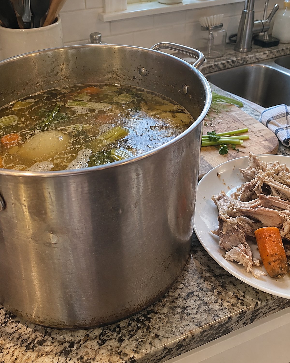 Cooked chicken bones and a carrot end sit beside a stockpot at the sink.