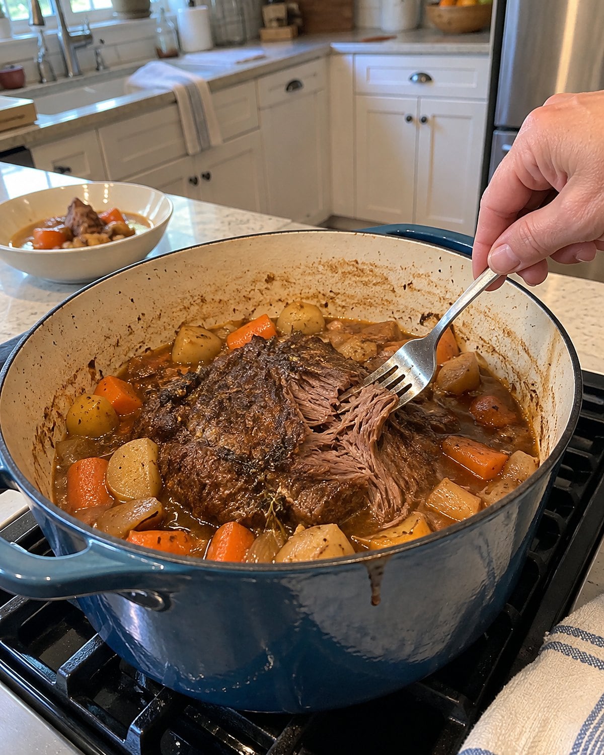 A fork rests in a tender chuck roast inside a Dutch oven on the stove.