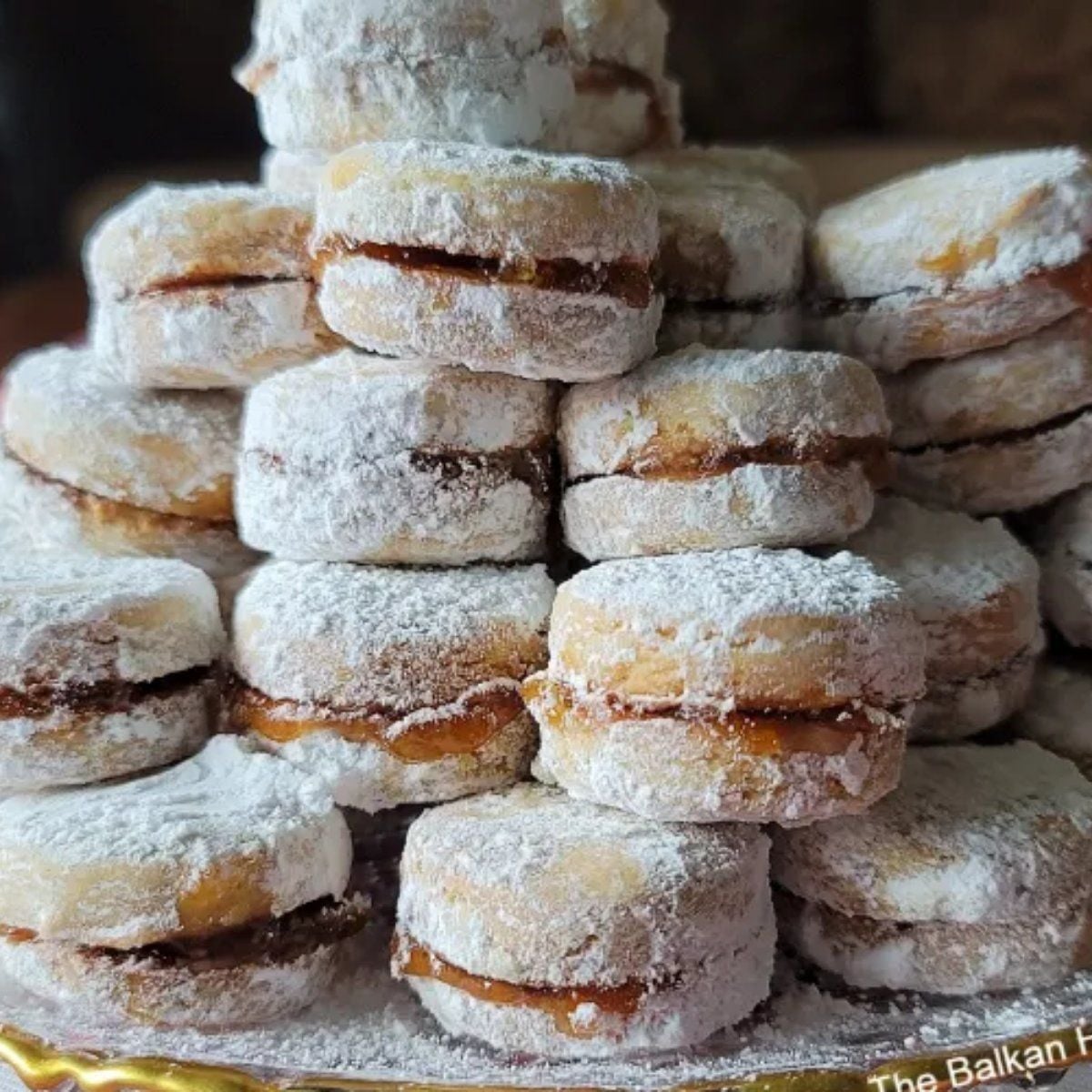 A stack of bite-sized Serbian Vanilice vanilla vanilla-walnut sandwich cookies filled with jam and generously coated in powdered sugar, served as a classic European Christmas dessert.