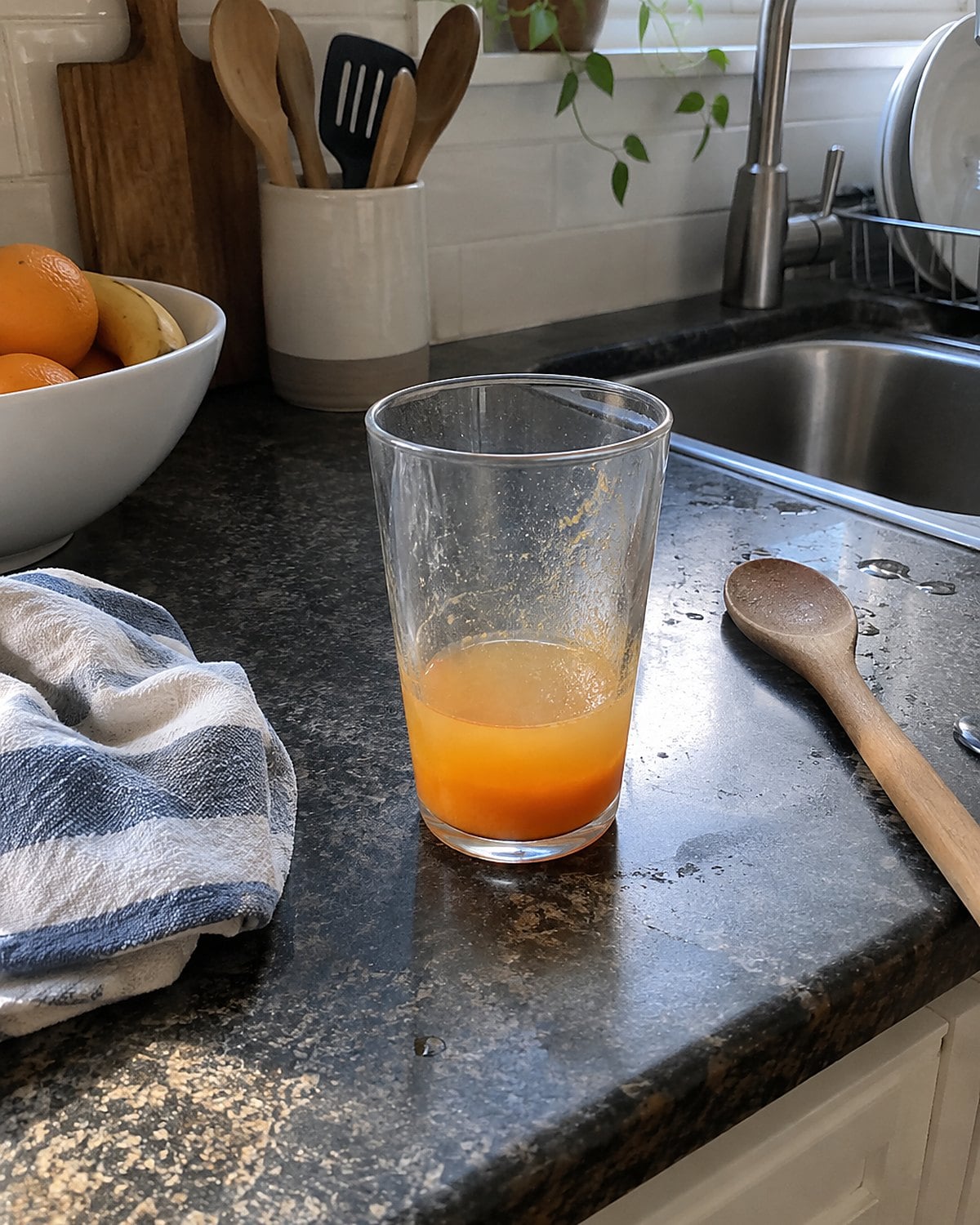 Orange drink mix settling at the bottom of a glass near the sink.