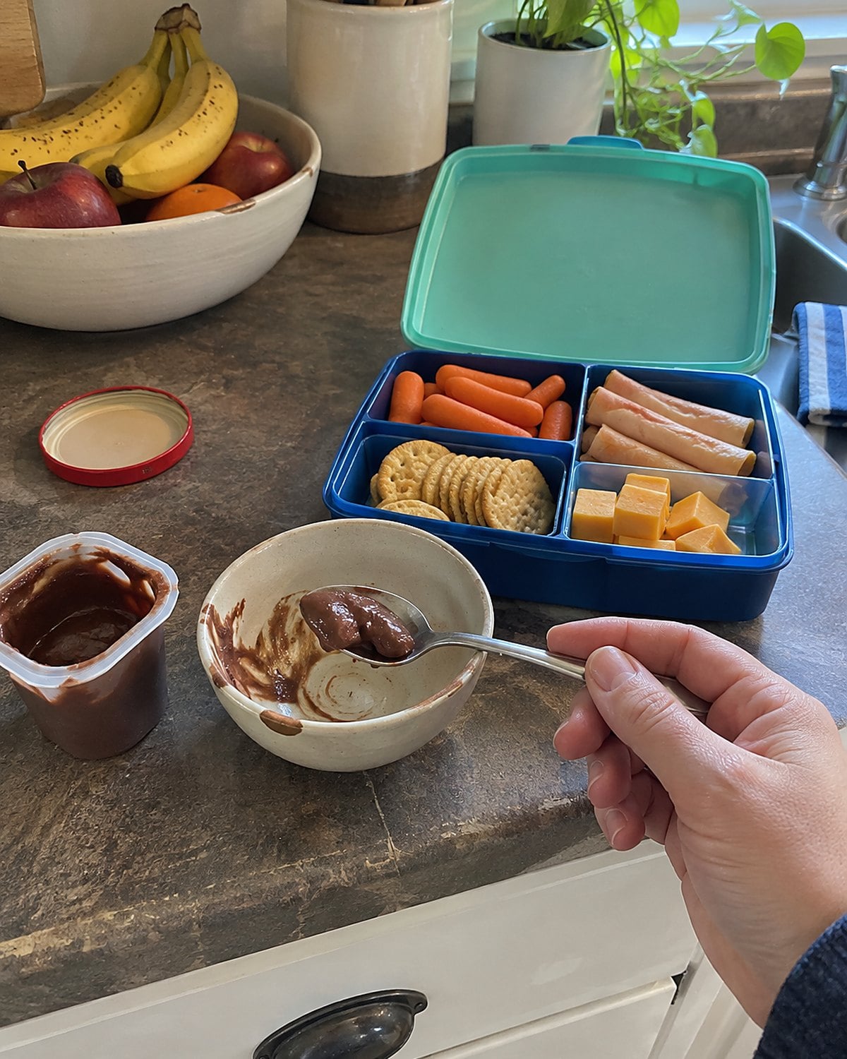 A plastic pudding cup and a small ceramic bowl beside a lunchbox on the counter.