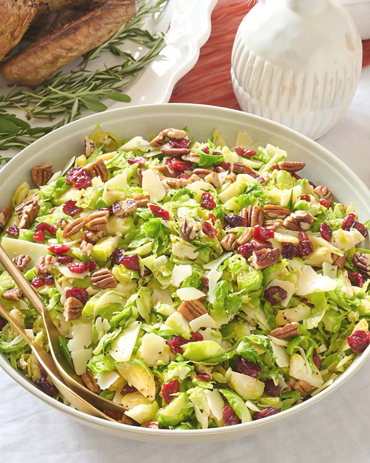 A large bowl of fresh shaved Brussels sprout salad tossed with dried cranberries, pecans, and shaved Parmesan cheese, ideal for Thanksgiving side dishes for a crowd.