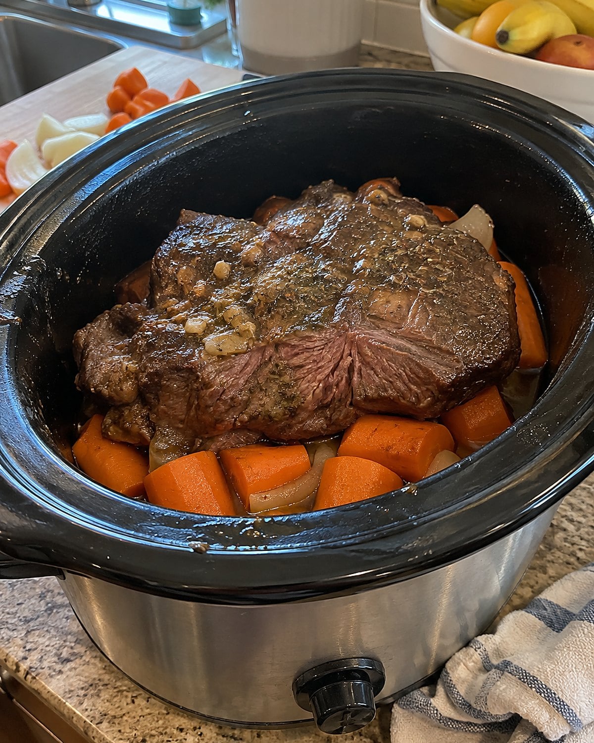 Thick carrot pieces at the bottom of an open crock with beef resting above them.