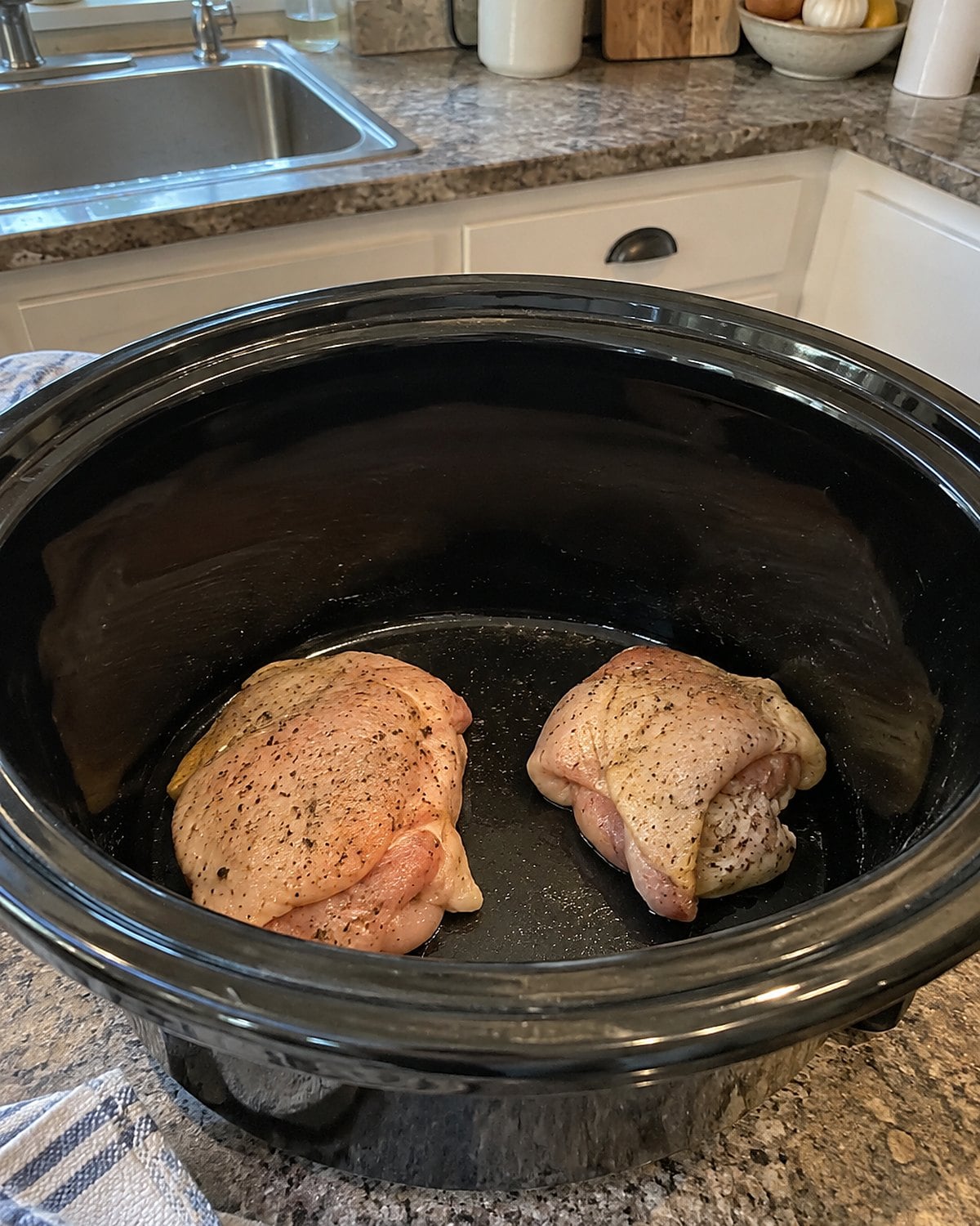 Two chicken thighs sitting in the broad bottom of an otherwise empty slow cooker crock.