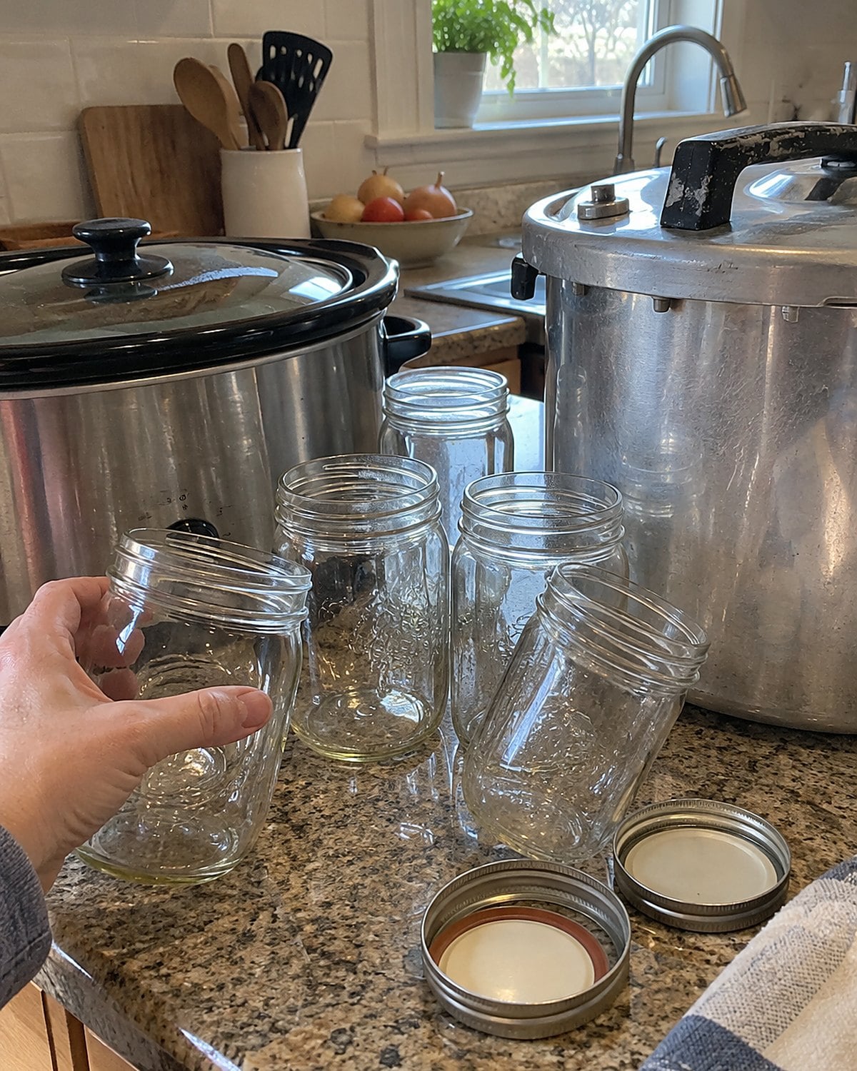 Empty canning jars beside a slow cooker and a separate pressure canner on a kitchen counter.