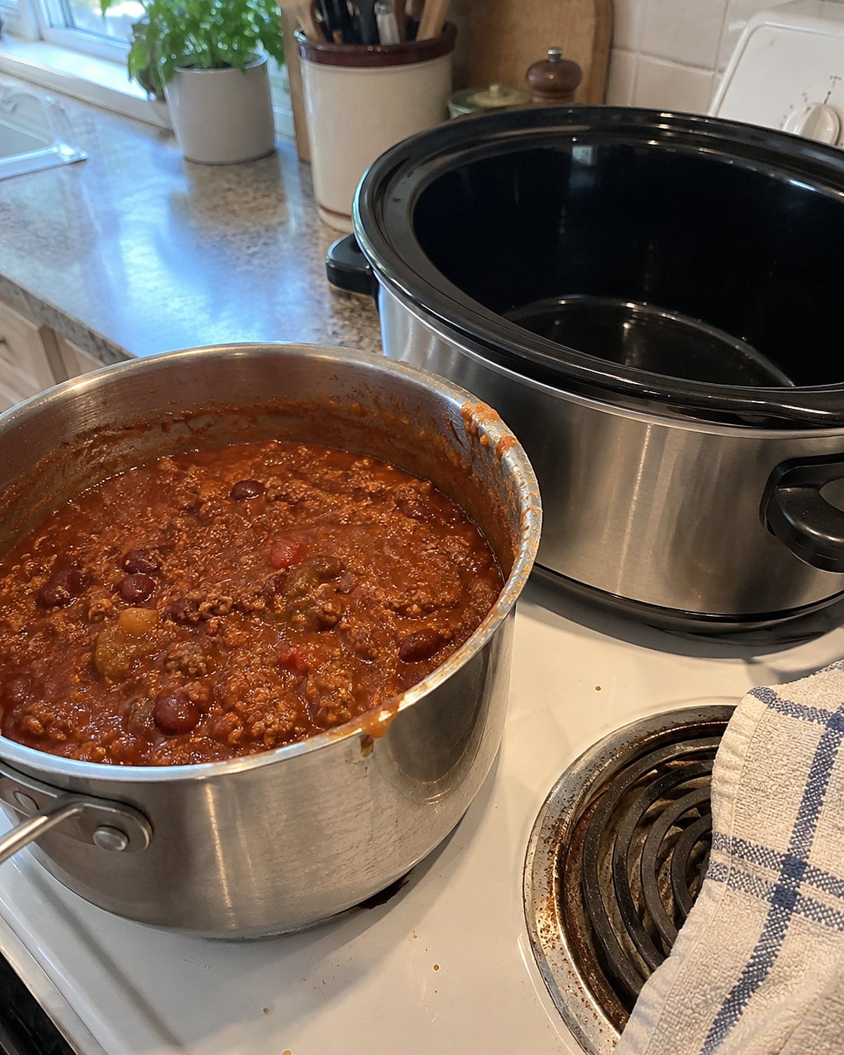 A saucepan of reheated chili beside an empty slow cooker on a white stove.