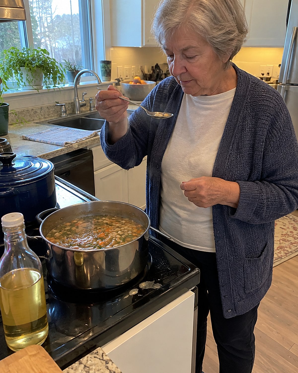 A hand testing a cooked bean beside a pot of bean soup and an unopened bottle of vinegar.