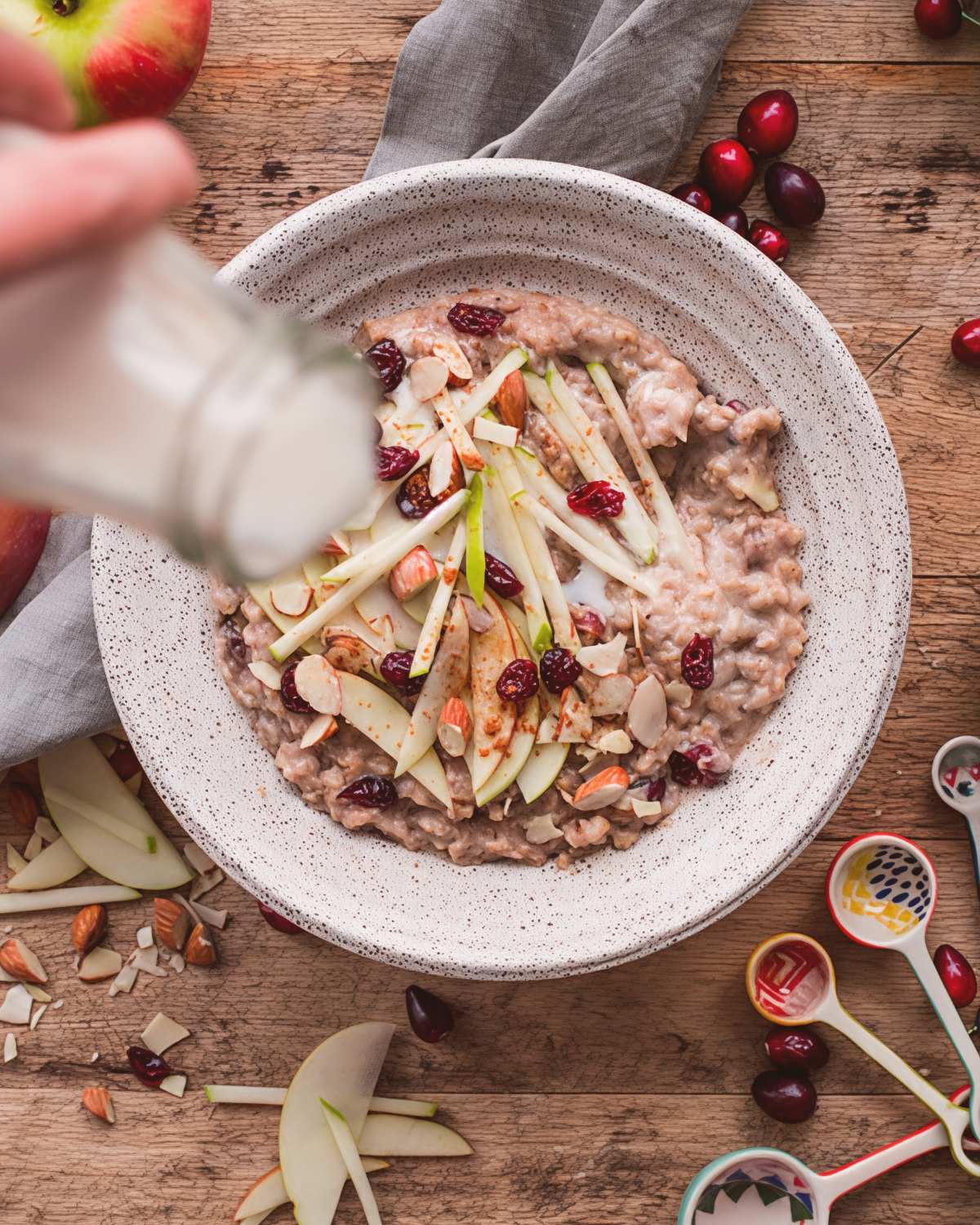 A bowl of slow cooker steel cut oats topped with fresh apple slices, cranberries, and almonds with milk being poured over it as Thanksgiving breakfast ideas.