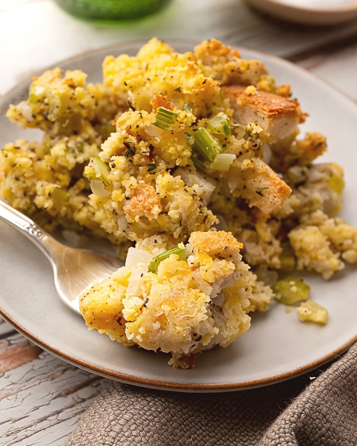 Southern cornbread dressing served on a plate with a fork, featuring savory herbs and celery as a traditional Thanksgiving side dish.