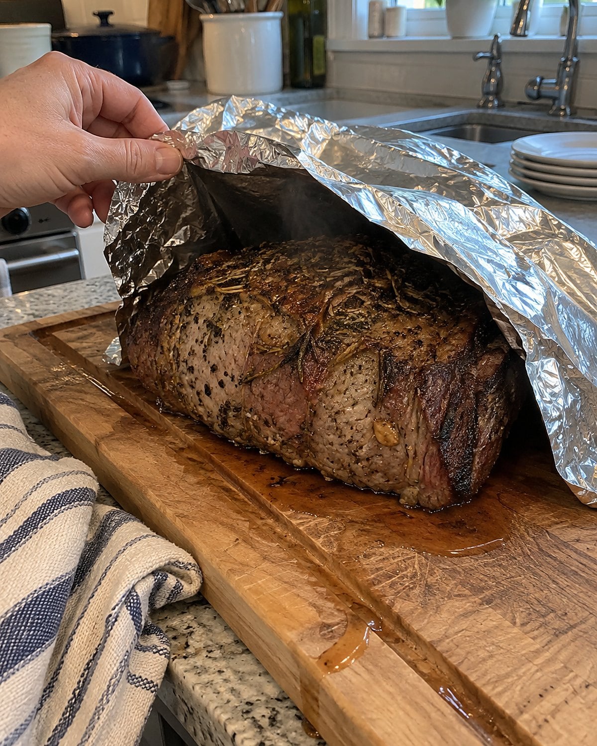 A roast resting under loose foil on a scarred wooden board.