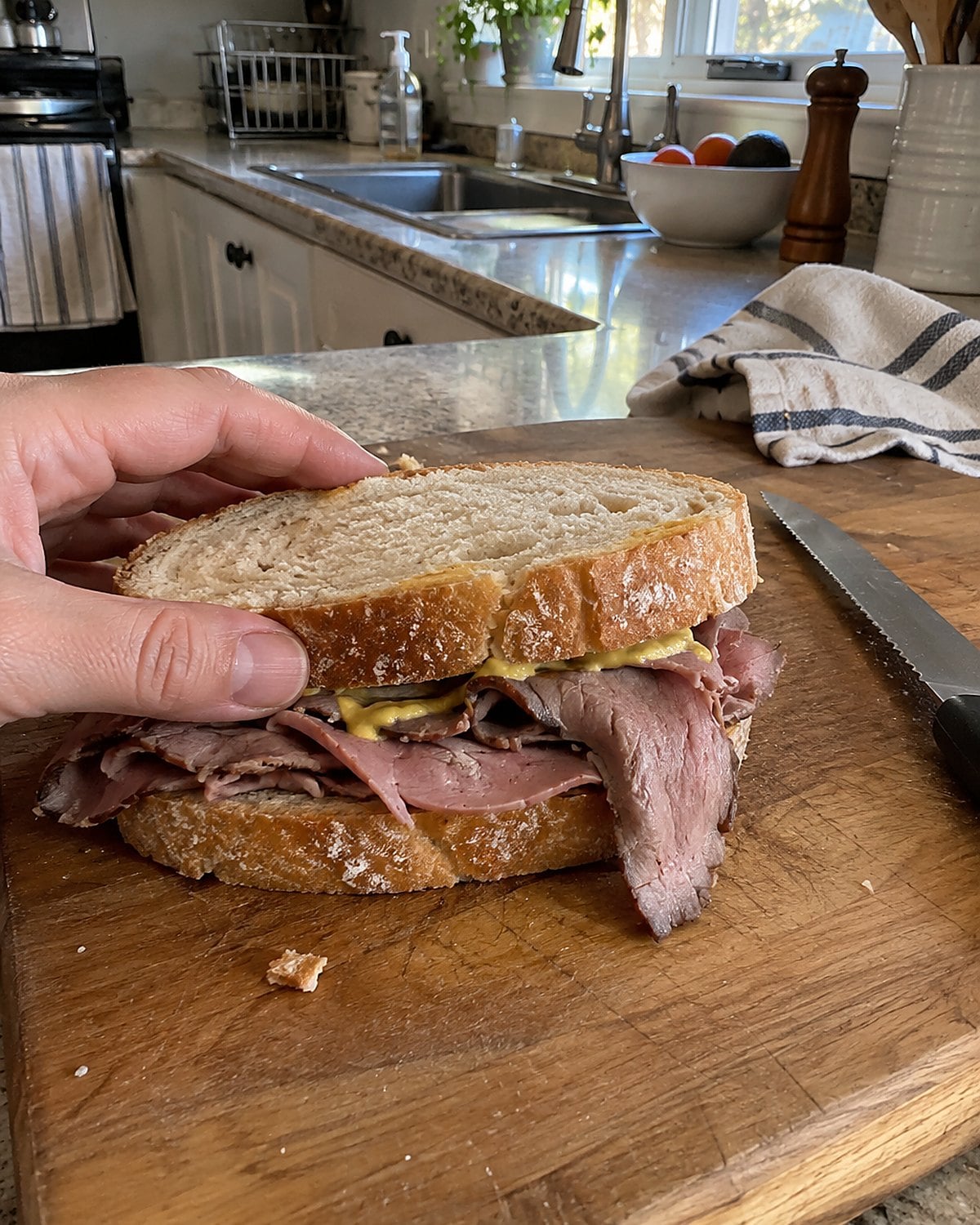Thin roast beef slices and mustard on bread at a kitchen counter.