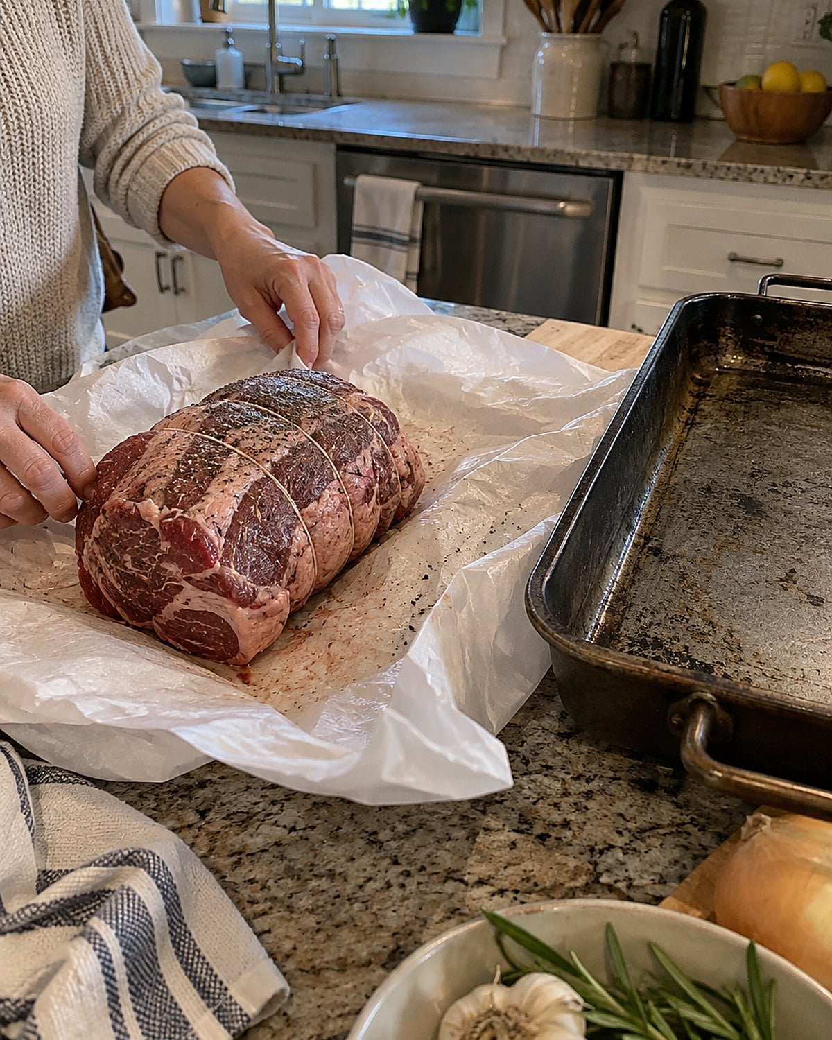 A small roast in opened butcher paper beside an old roasting pan on a kitchen counter.