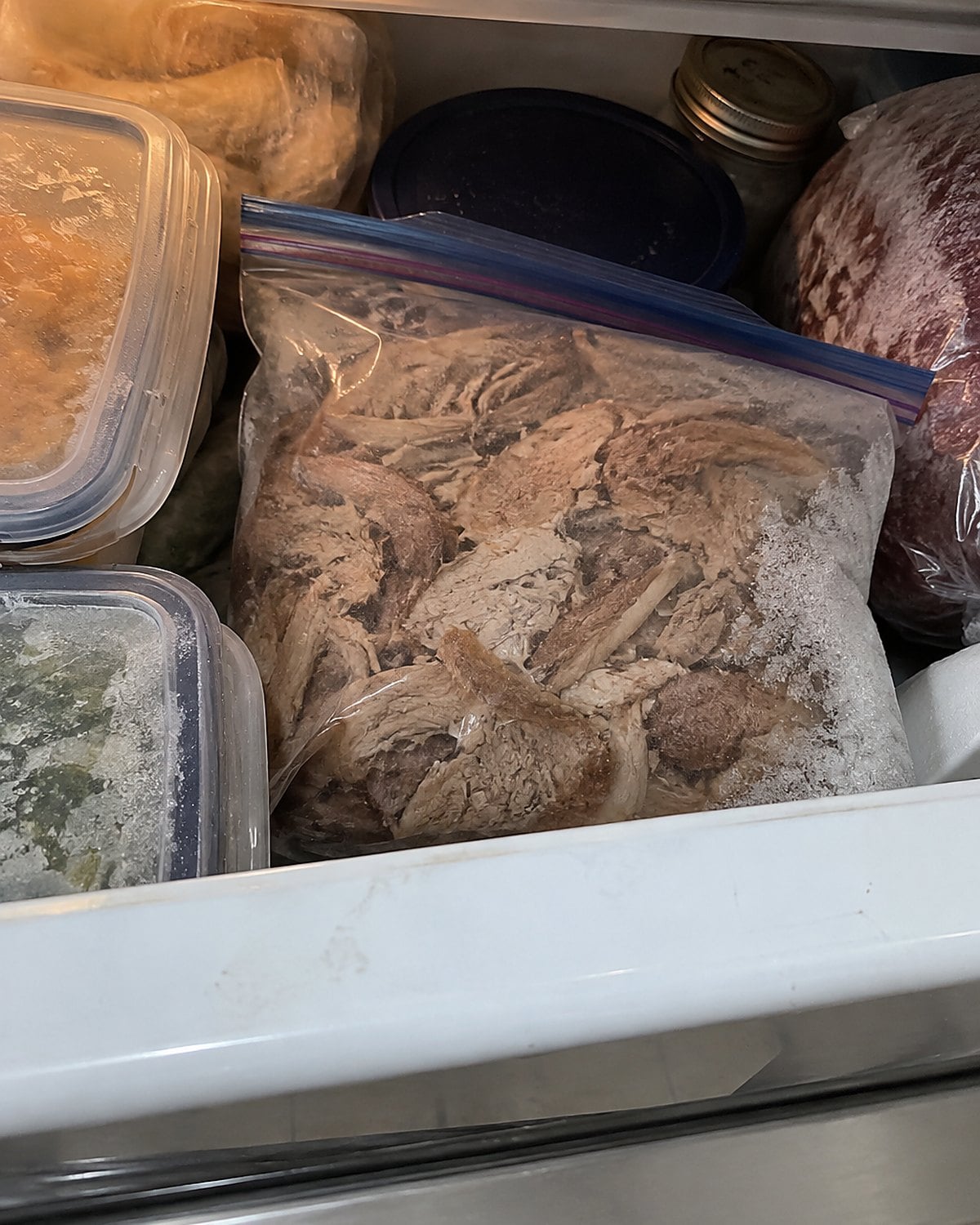 A dated freezer bag of cooked roast tucked into a crowded freezer drawer.