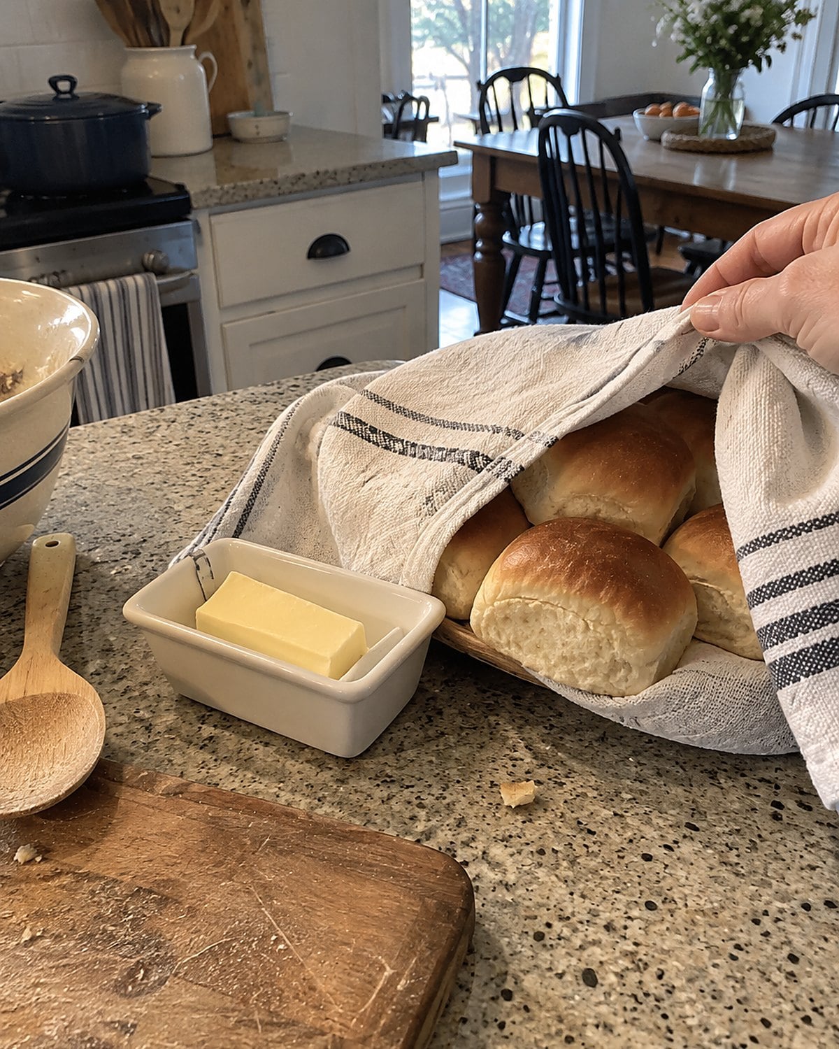 Dinner rolls under a clean towel beside a small butter dish.