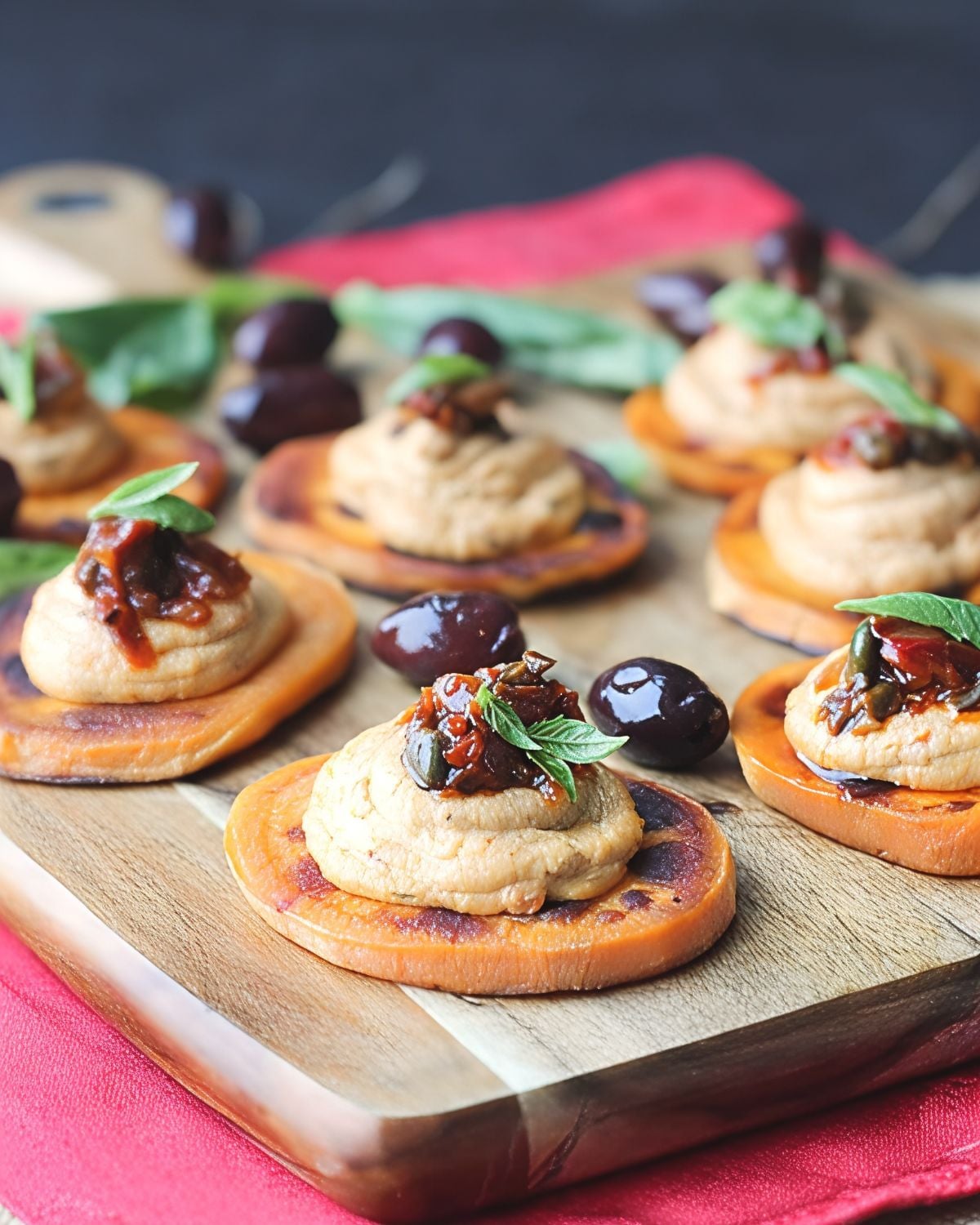 Roasted sweet potato rounds topped with creamy spread, sun-dried tomatoes, and fresh basil leaves, ideal for vegan Thanksgiving appetizers.