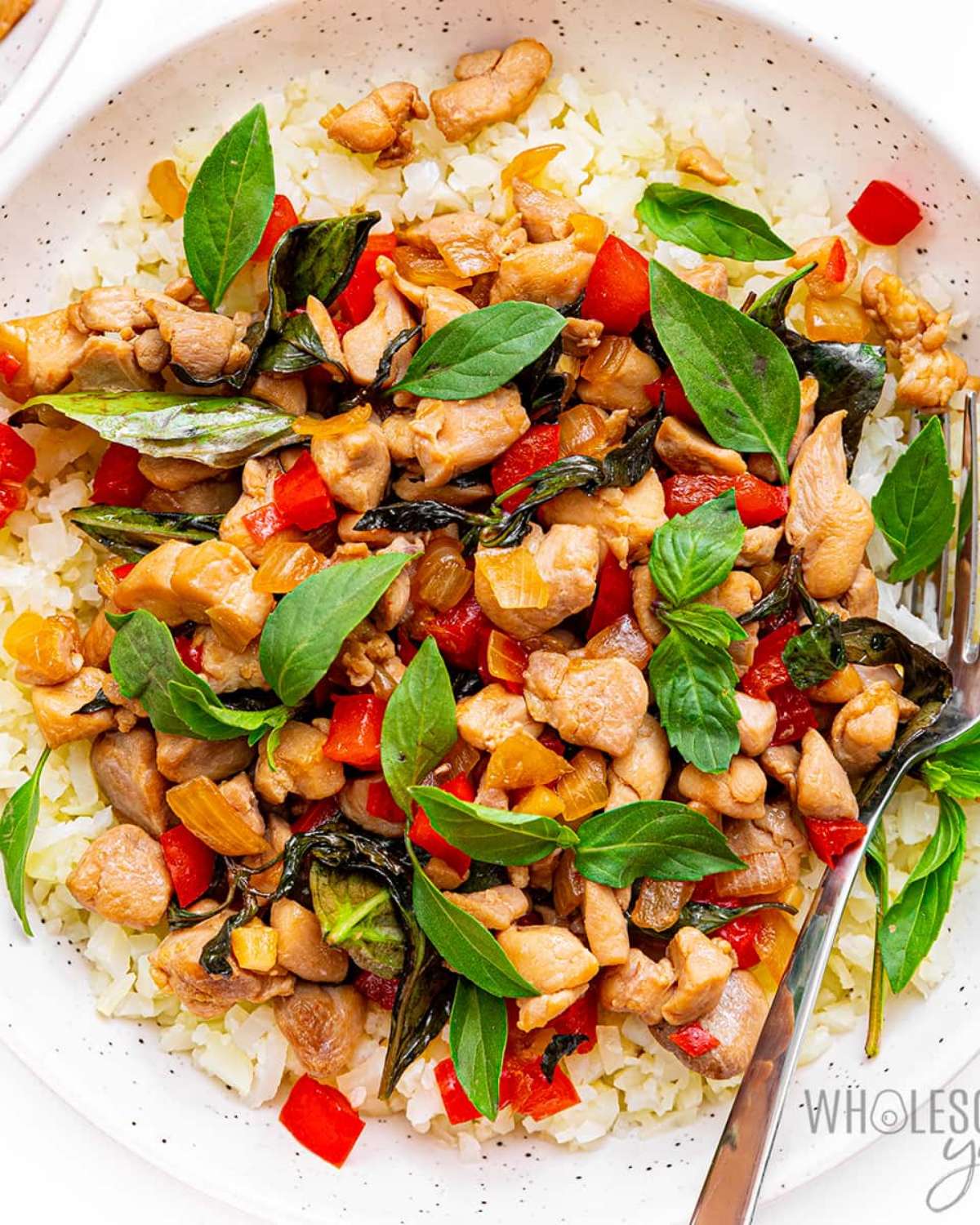 A close-up view of aromatic Thai Basil Chicken with glossy glaze and vibrant green leaves served over a low-carb base, featured as a delicious high protein low carb recipes dinner