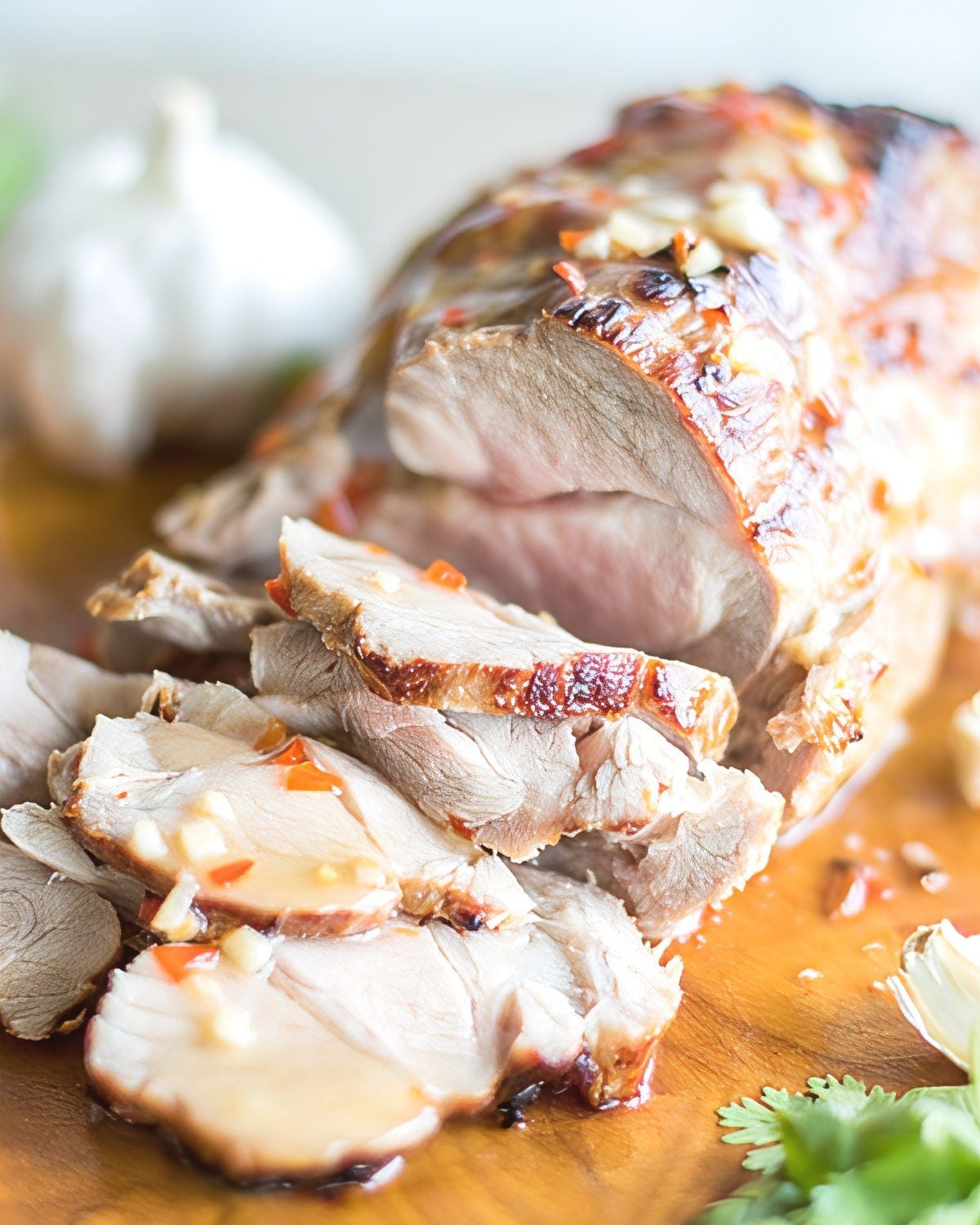 Sliced Thai sweet chili pork roast with garlic and glaze on a wooden board