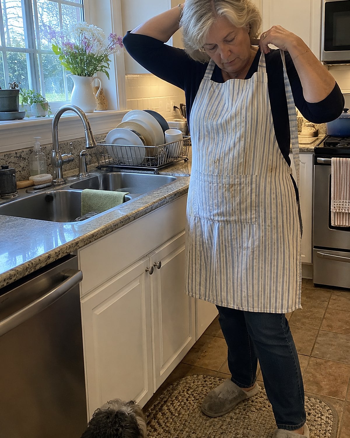 An older womanโs hands taking off a stained apron beside the sink before washing up.