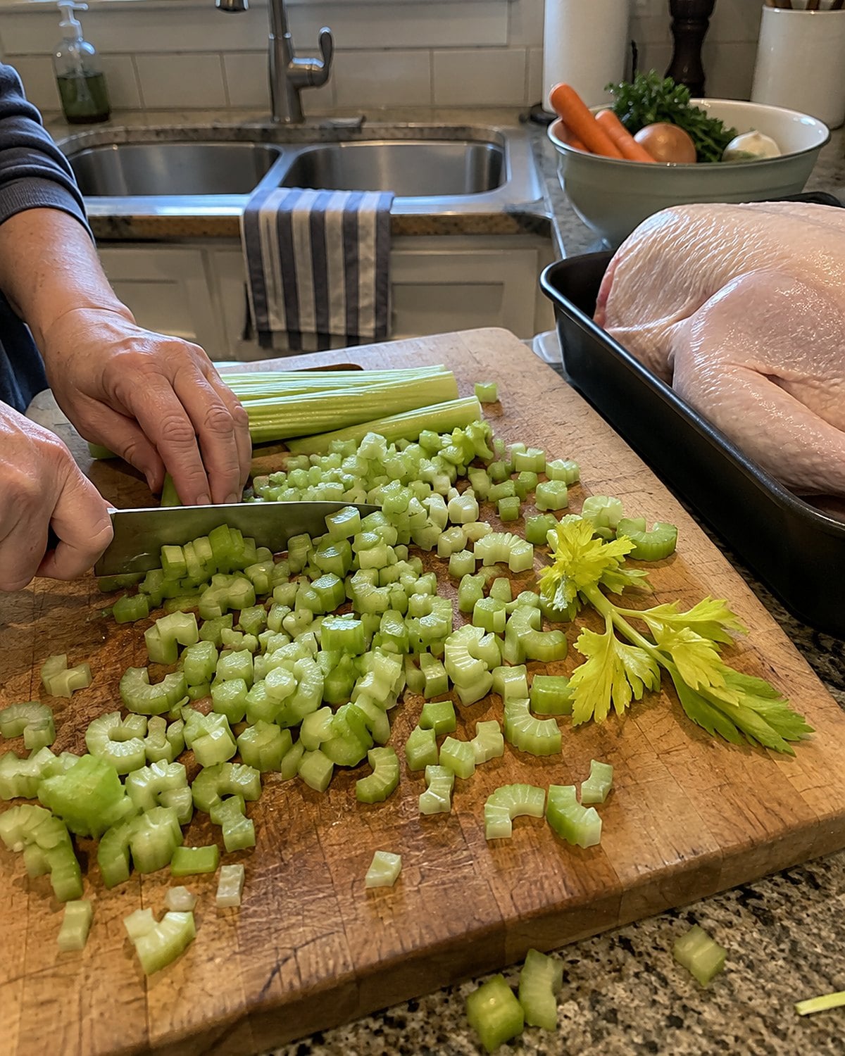 A board of chopped celery beside a separate tray holding a wrapped raw turkey on the kitchen counter.