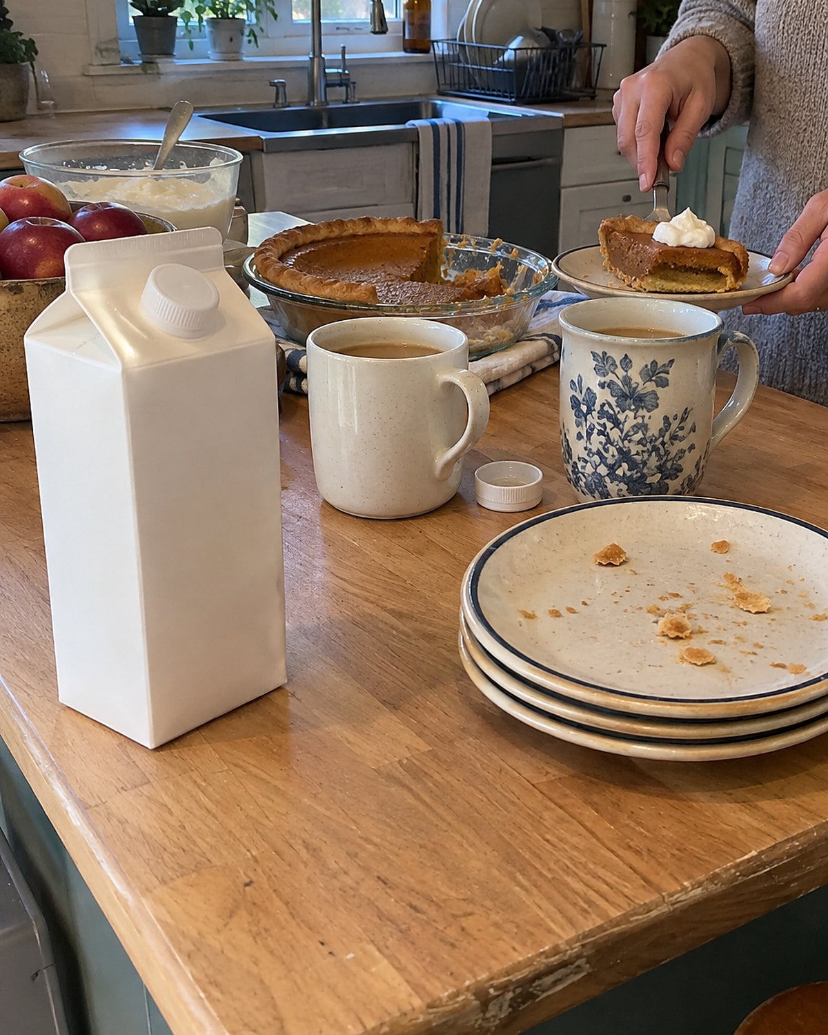 A carton of cream beside two coffee mugs and a stack of dessert plates.