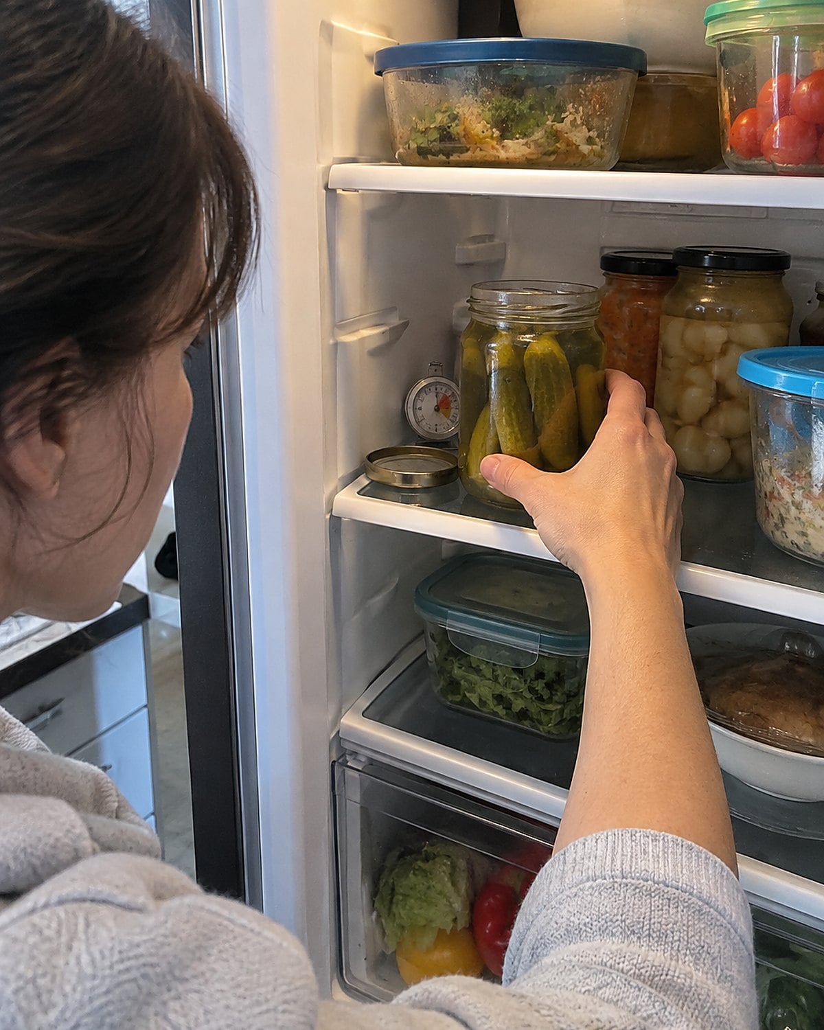 A small refrigerator thermometer tucked behind a pickle jar on a full shelf.