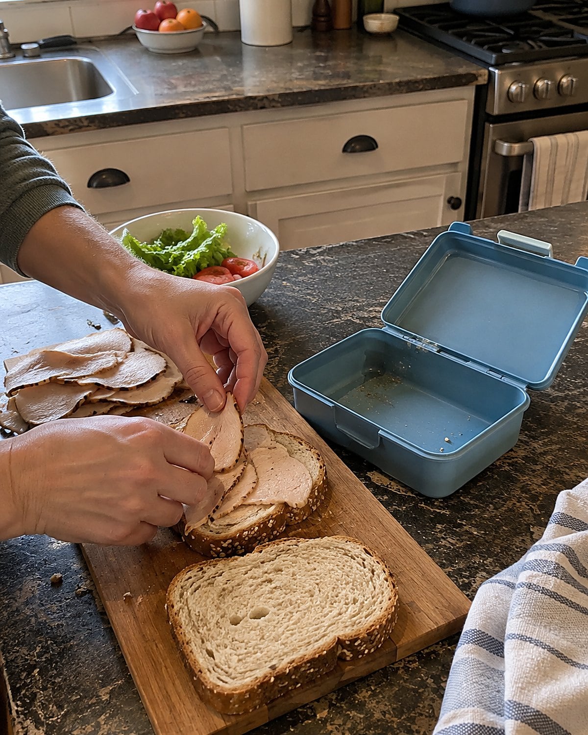 Sliced turkey and bread beside an open lunch box on a kitchen counter.