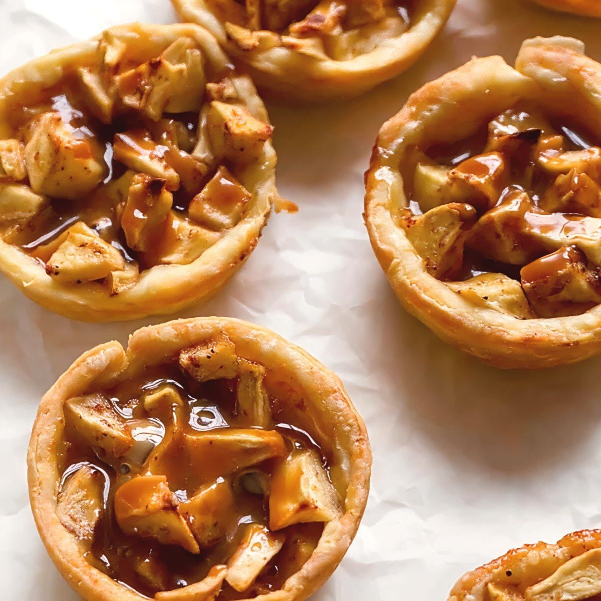 Golden-brown mini caramel apple pies filled with diced spiced apples and rich caramel drizzle, perfect individual treats for Thanksgiving potluck desserts.