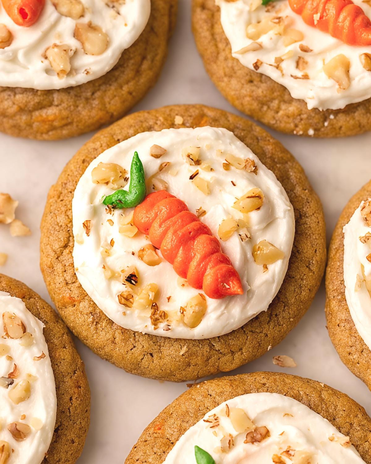 Soft vegan carrot cake cookies topped with creamy white frosting, chopped walnuts, and a cute piped icing carrot, perfect for Thanksgiving potluck desserts.