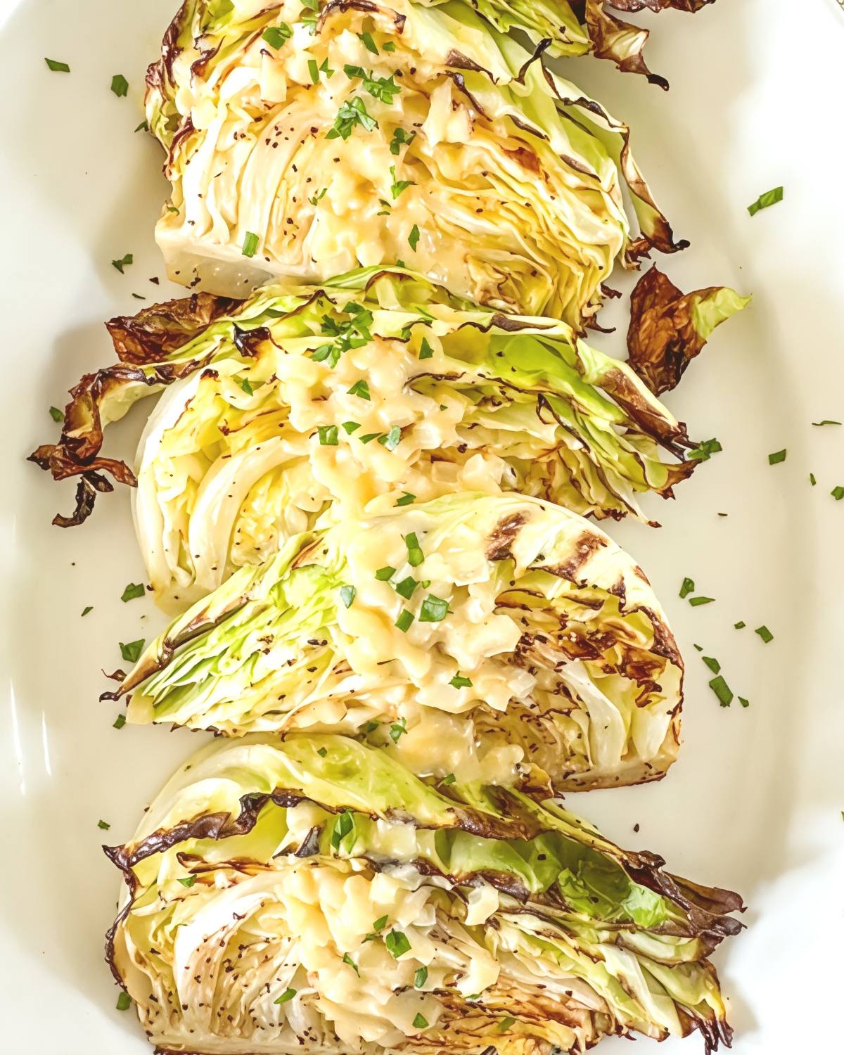 Tender roasted cabbage wedges drizzled with creamy onion Dijon sauce and garnished with fresh herbs, served on a white platter for Thanksgiving side dishes for a crowd.
