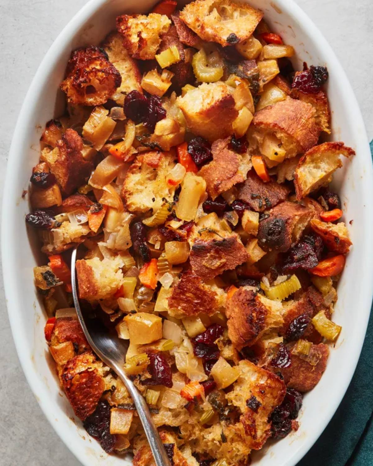 Golden baked vegetarian stuffing with toasted bread cubes, dried cranberries, celery, and carrots in a white oval baking dish, perfect for Thanksgiving side dishes for a crowd.