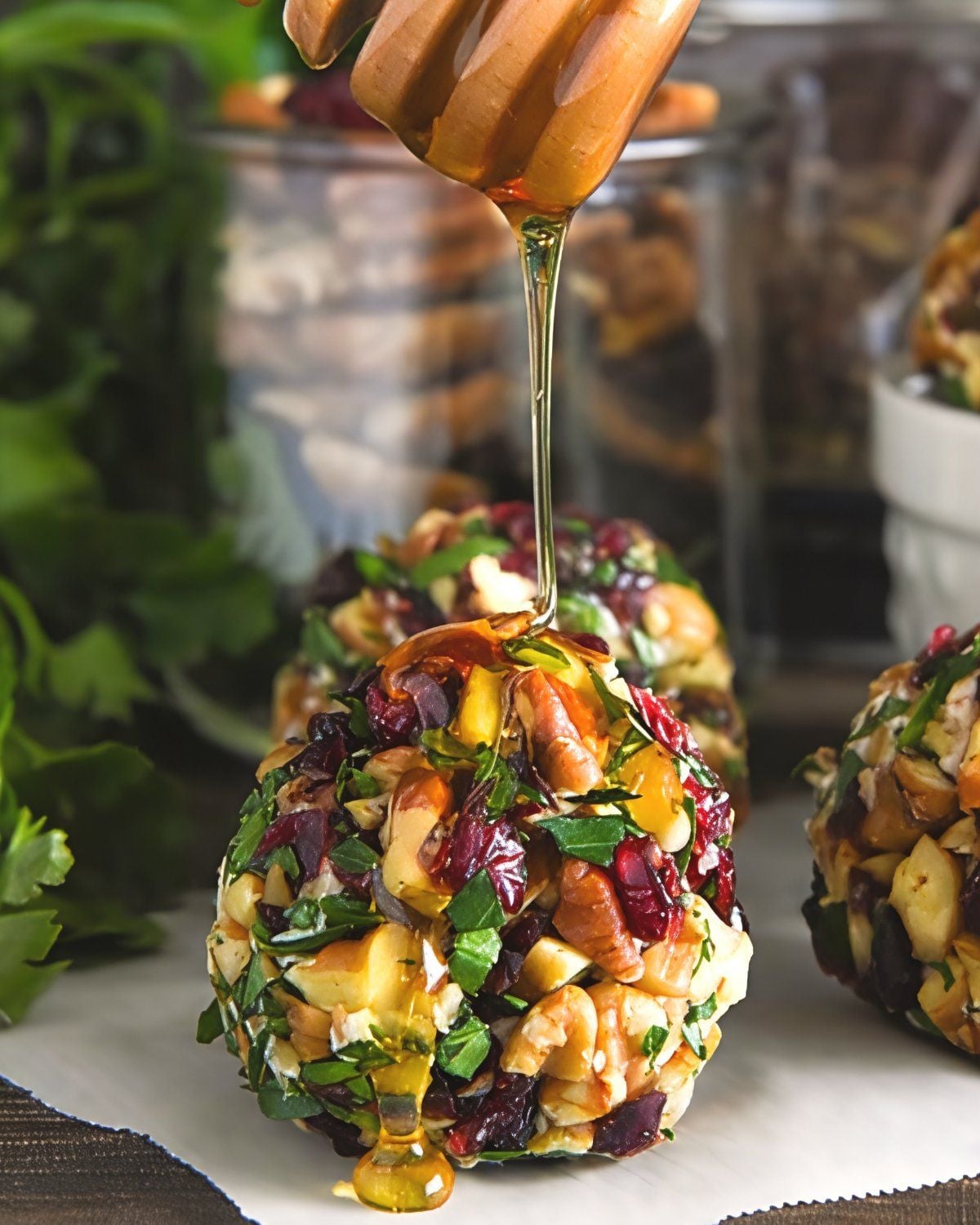 Golden honey drizzled from a wooden dipper onto mini goat cheese balls coated in chopped pecans, dried cranberries, and fresh herbs makes for festive Thanksgiving Snacks Appetizers.