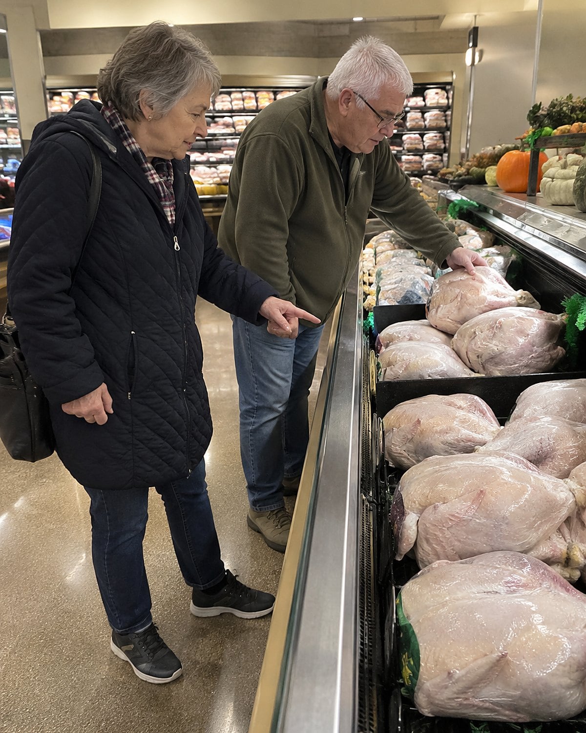 A shopper's hands point toward smaller turkeys in a market case.