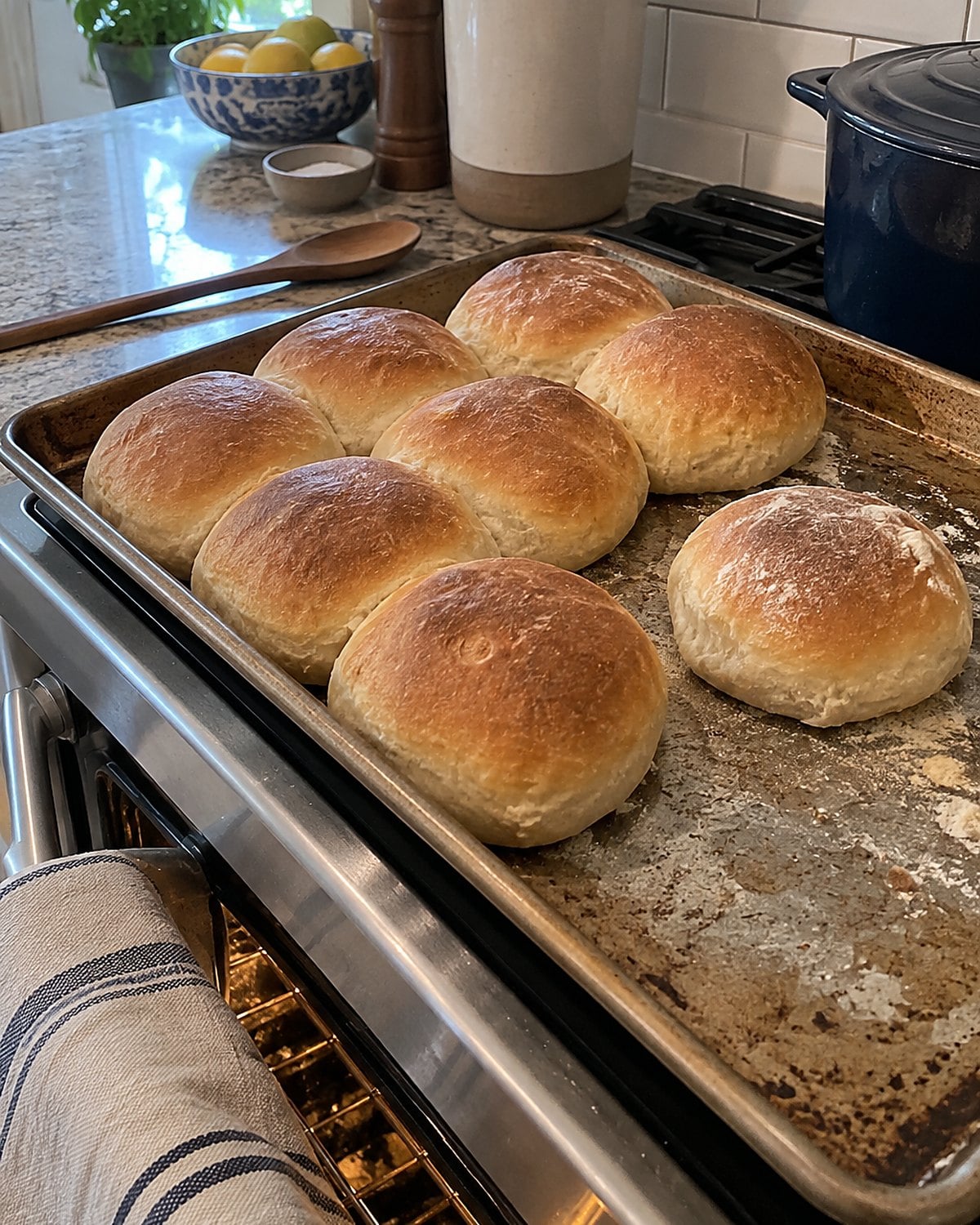 Uneven rolls rise on a crowded baking sheet beside the oven.