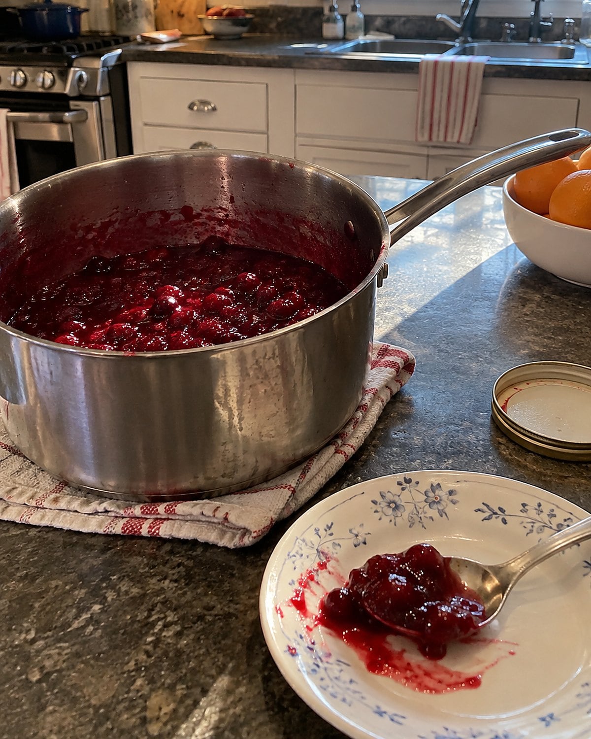 A spoonful of cranberry sauce cools on a saucer beside a worn saucepan.