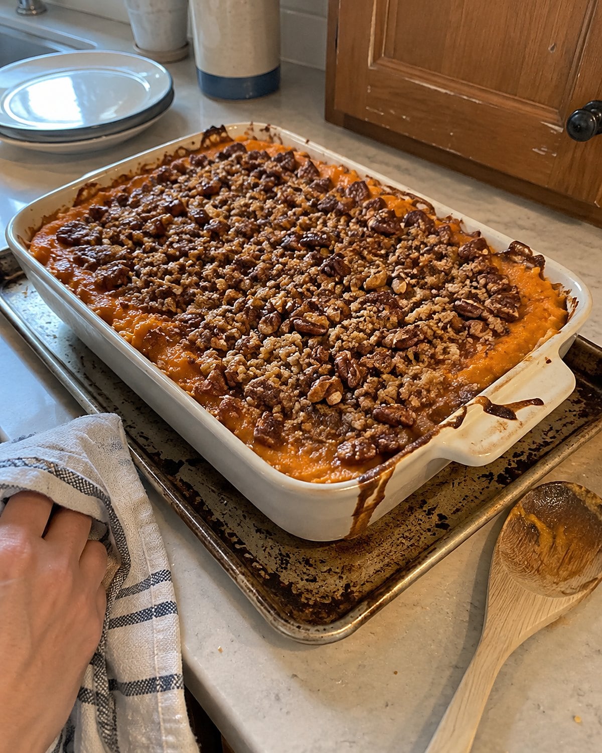 Sweet potato casserole fills a baking dish near its rim on a stained sheet pan.