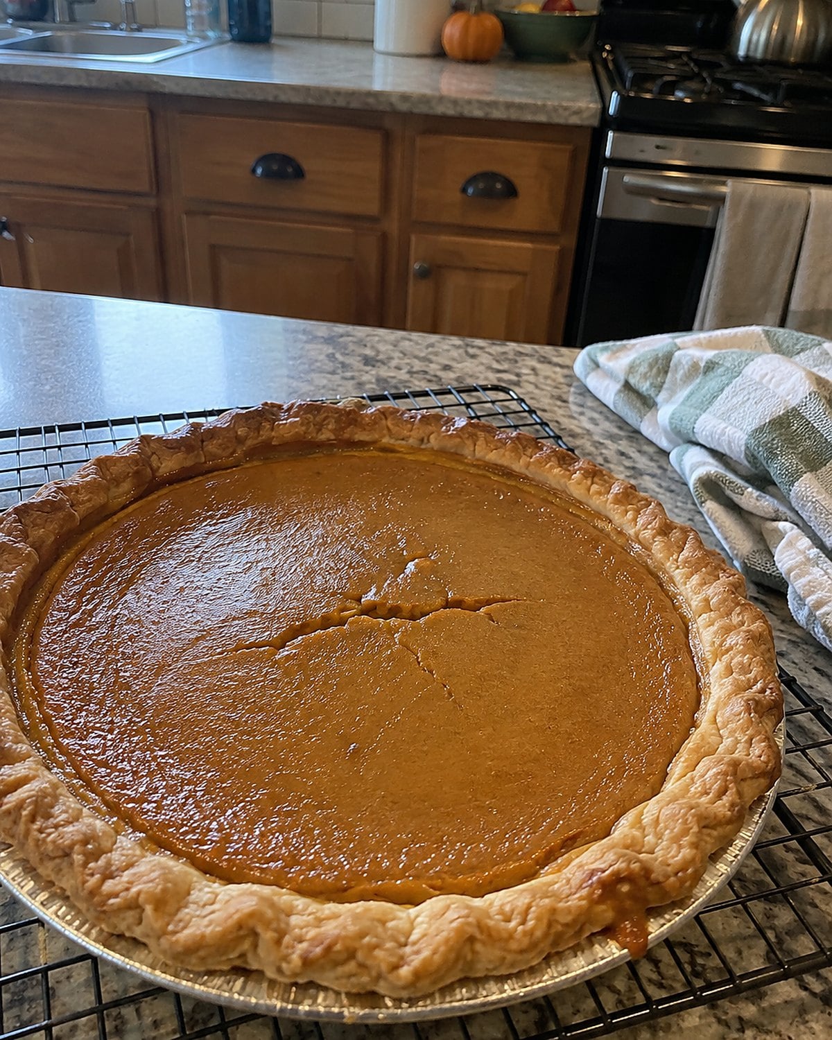 A slightly cracked pumpkin pie cools in its pan on a wire rack.