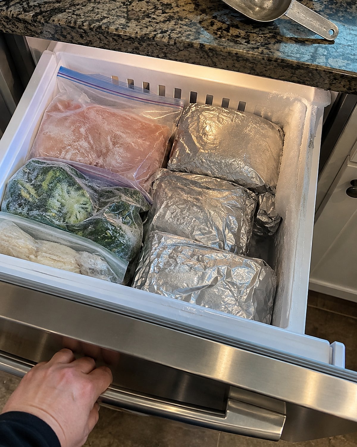 A freezer drawer holds silver foil packets beside a few dated freezer bags.