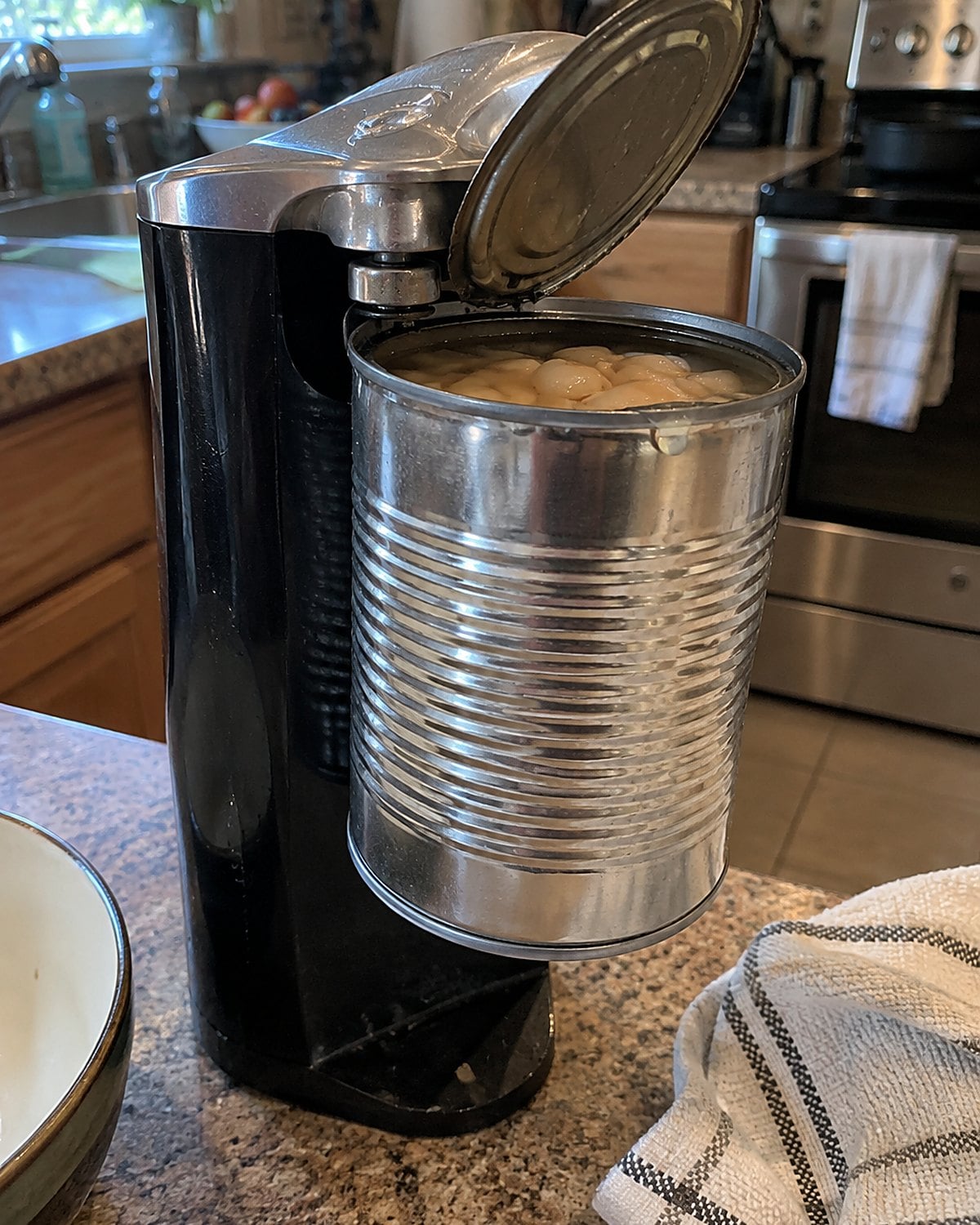 A countertop electric can opener holds an opened can above a chipped kitchen counter.
