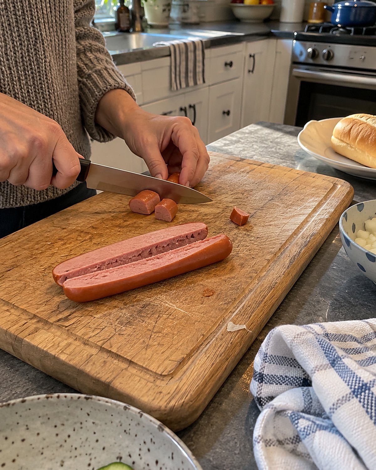 A hot dog split lengthwise on a cutting board, with small pieces beside the knife.