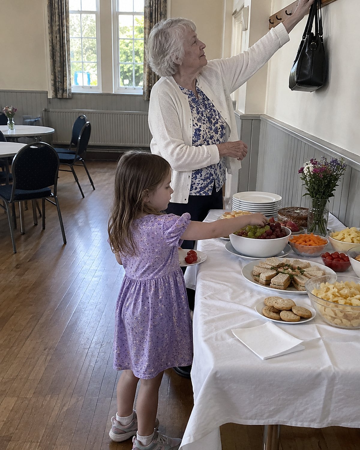 A zipped handbag hanging above a child’s reach beside a church hall snack table.