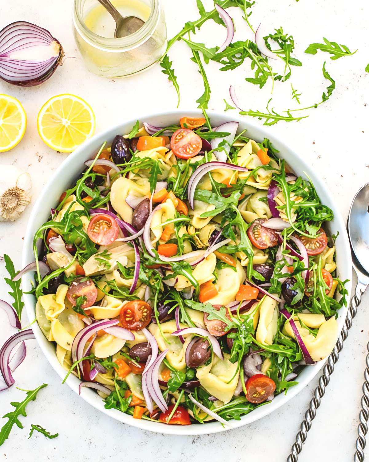 Vibrant tortellini pasta salad tossed with cherry tomatoes, Kalamata olives, sliced red onion, and fresh arugula in a large serving bowl, ideal for quick and easy last minute potluck ideas.