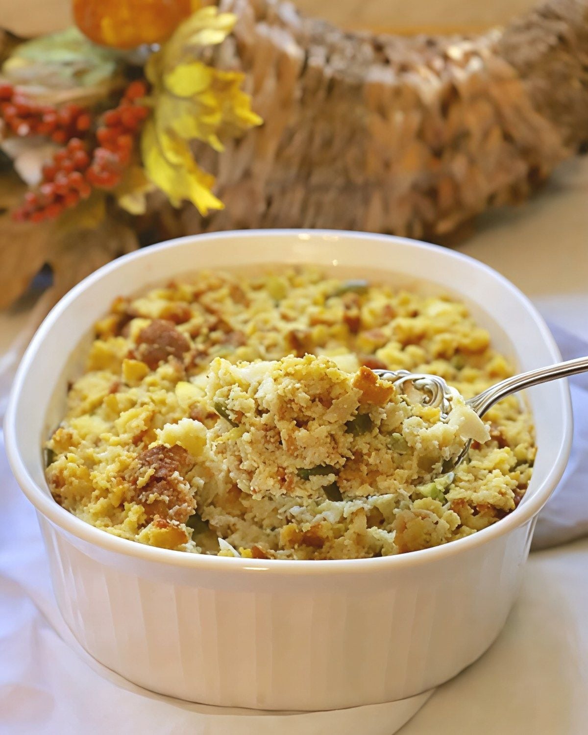 Traditional Southern cornbread dressing in a white serving dish being scooped with a spoon as a classic Thanksgiving side dish.