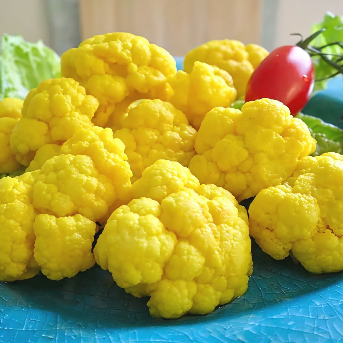 Vibrant yellow turmeric pickled cauliflower florets arranged on a platter with fresh greens and a cherry tomato for a healthy and light Thanksgiving appetizer.